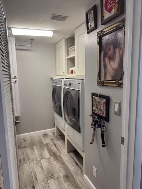 laundry area with washer and clothes dryer, light hardwood / wood-style floors, and cabinets