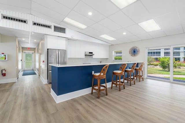 kitchen featuring stainless steel fridge, light wood-type flooring, white cabinetry, kitchen peninsula, and a breakfast bar area