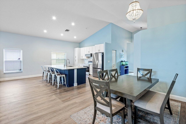 dining room with sink, high vaulted ceiling, a notable chandelier, and light wood-type flooring