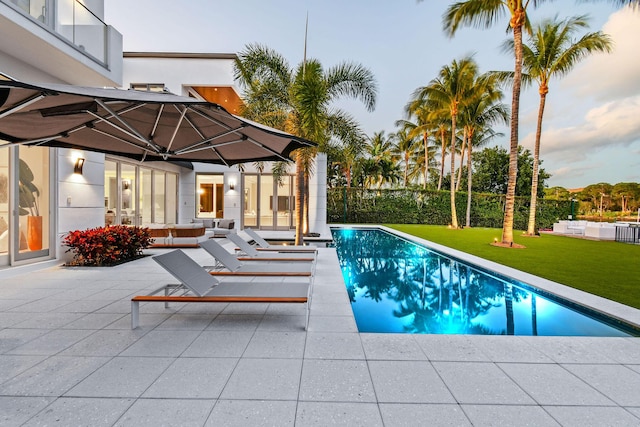 pool at dusk with a yard and a patio