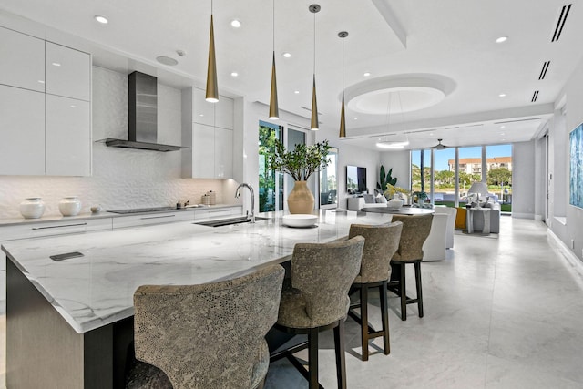 kitchen featuring white cabinets, hanging light fixtures, wall chimney exhaust hood, a large island, and a kitchen bar