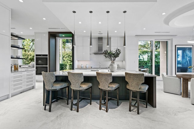 kitchen with a large island, white cabinets, pendant lighting, and wall chimney range hood