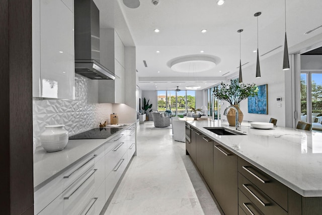 kitchen featuring a large island, sink, wall chimney range hood, decorative light fixtures, and black electric cooktop