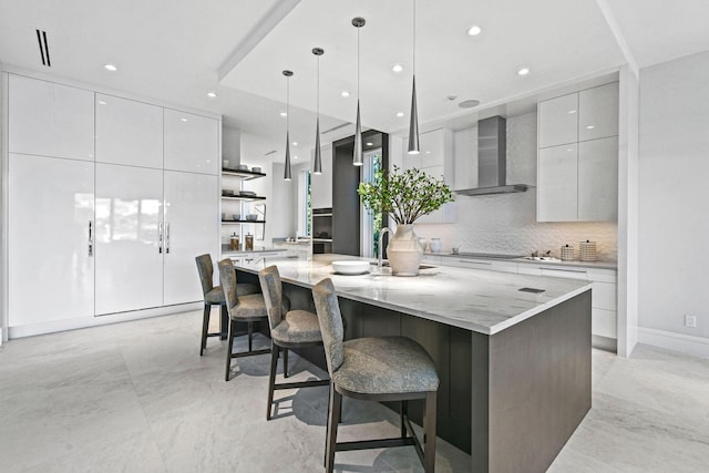 kitchen featuring a large island with sink, a breakfast bar, wall chimney exhaust hood, and decorative light fixtures