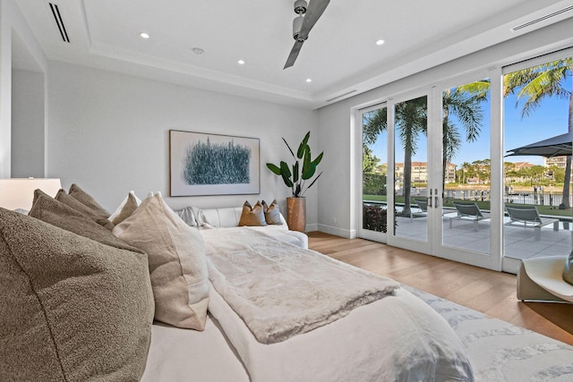 bedroom featuring french doors, access to outside, light hardwood / wood-style flooring, and a tray ceiling