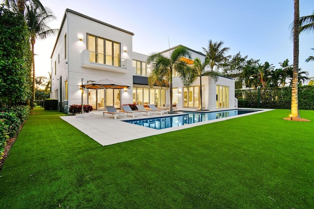 back house at dusk with a fenced in pool, a lawn, and a patio