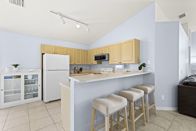 kitchen featuring kitchen peninsula, light brown cabinets, white appliances, and a breakfast bar area