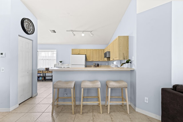 kitchen featuring kitchen peninsula, light brown cabinetry, vaulted ceiling, white refrigerator, and a breakfast bar area