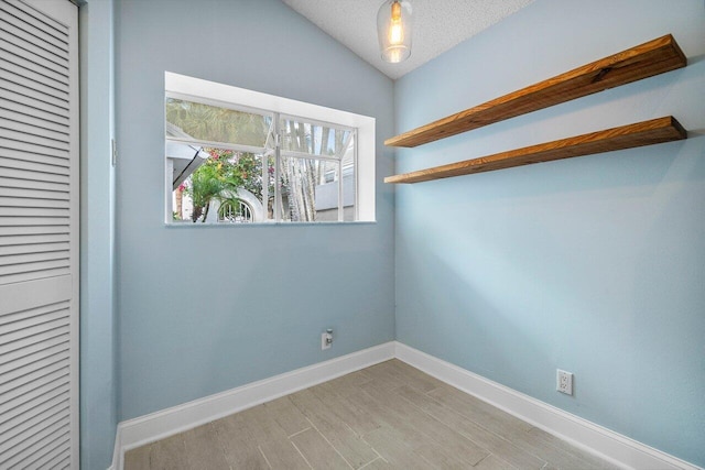 spare room featuring lofted ceiling, a textured ceiling, and light hardwood / wood-style floors