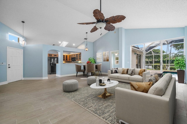 living room featuring a textured ceiling, high vaulted ceiling, ceiling fan, and light wood-type flooring