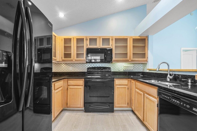 kitchen with tasteful backsplash, lofted ceiling, sink, dark stone countertops, and black appliances