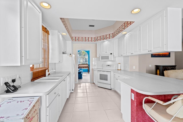 kitchen with light tile patterned floors, kitchen peninsula, white appliances, white cabinets, and sink