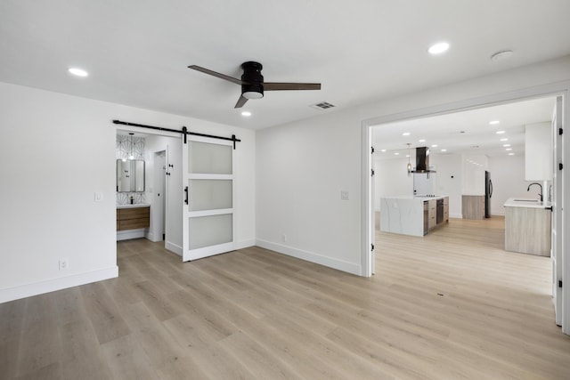interior space with visible vents, a ceiling fan, a sink, a barn door, and light wood finished floors