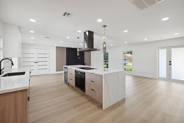 kitchen with light wood finished floors, island exhaust hood, black appliances, modern cabinets, and a sink