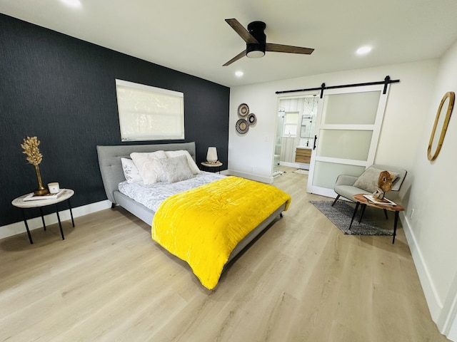 bedroom featuring baseboards, light wood finished floors, recessed lighting, an accent wall, and a barn door
