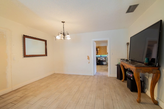 empty room with a notable chandelier, visible vents, light wood-style floors, a textured ceiling, and baseboards