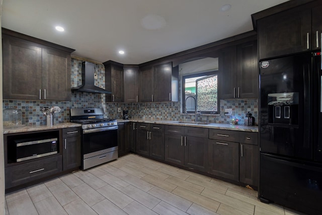 kitchen with light stone countertops, stainless steel appliances, a sink, wall chimney range hood, and decorative backsplash