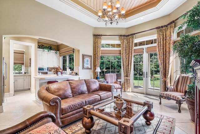 tiled living room with a raised ceiling, crown molding, french doors, and a chandelier