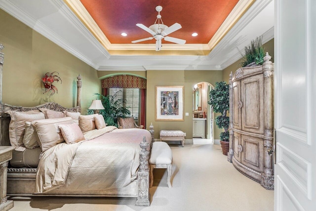 carpeted bedroom with connected bathroom, a tray ceiling, ceiling fan, and ornamental molding