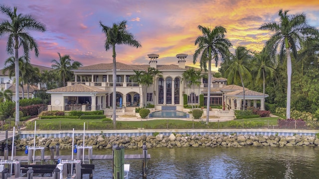 back house at dusk with a patio, a balcony, and a water view