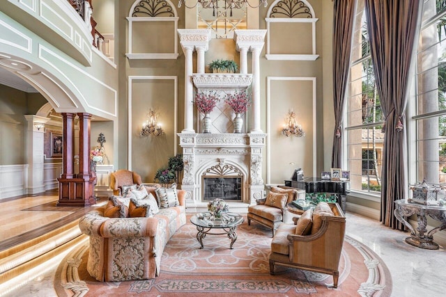 living room with a fireplace, a towering ceiling, decorative columns, and ornamental molding