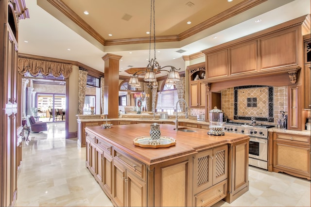 kitchen with high end range, sink, hanging light fixtures, ornate columns, and an island with sink