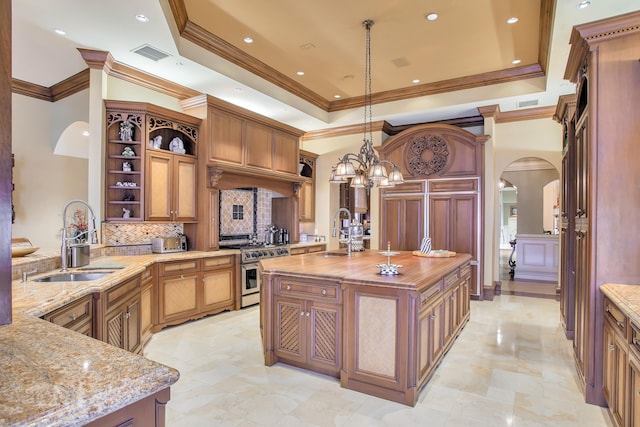 kitchen featuring decorative light fixtures, a center island with sink, high end stainless steel range oven, and sink