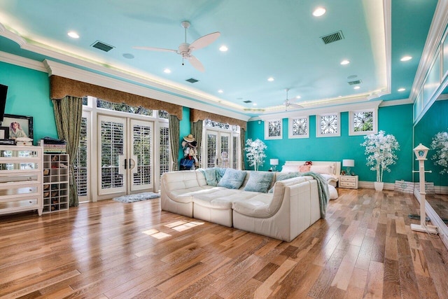 living room with a tray ceiling, french doors, ornamental molding, and light wood-type flooring