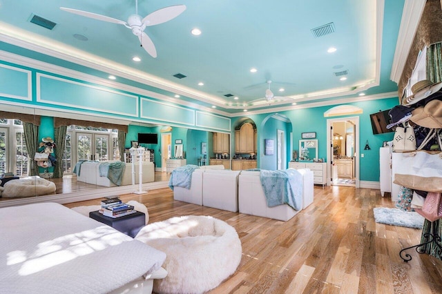 living room with french doors, light wood-type flooring, a raised ceiling, ceiling fan, and crown molding