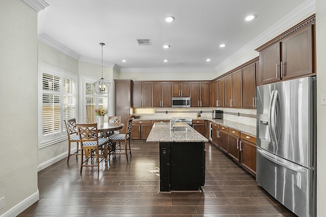 kitchen featuring light stone countertops, appliances with stainless steel finishes, ornamental molding, a kitchen island with sink, and hanging light fixtures