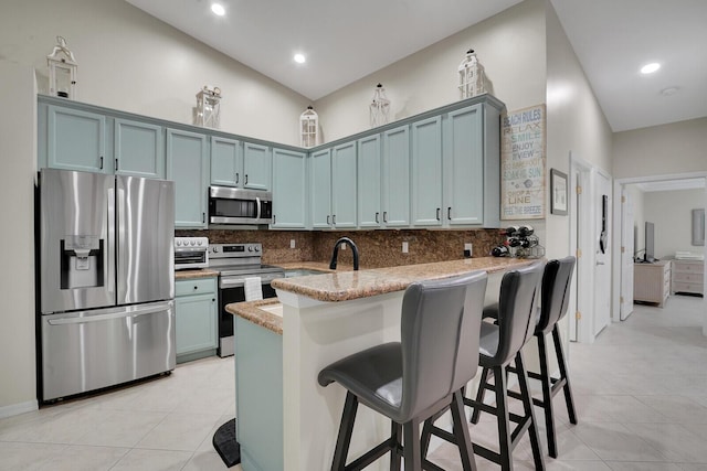 kitchen featuring a peninsula, a kitchen breakfast bar, appliances with stainless steel finishes, blue cabinetry, and decorative backsplash