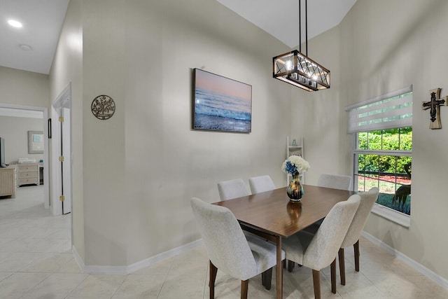 dining space featuring a towering ceiling, baseboards, a chandelier, and light tile patterned floors
