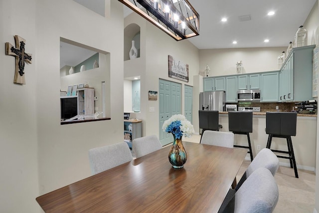 dining room with a notable chandelier, light tile patterned floors, recessed lighting, visible vents, and a high ceiling