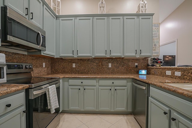 kitchen featuring tasteful backsplash, stainless steel appliances, dark stone countertops, and light tile patterned flooring