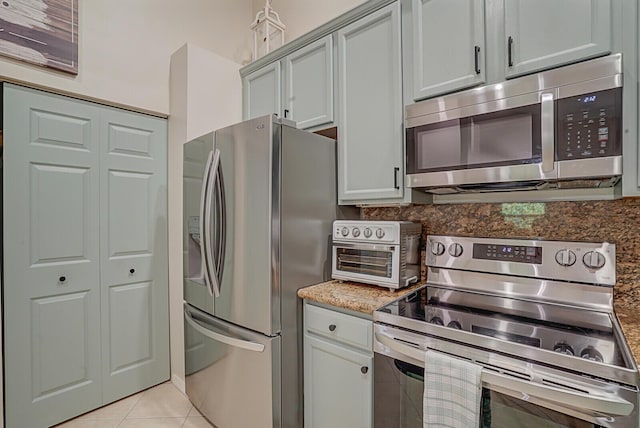 kitchen featuring light tile patterned floors, a toaster, decorative backsplash, light stone countertops, and stainless steel appliances