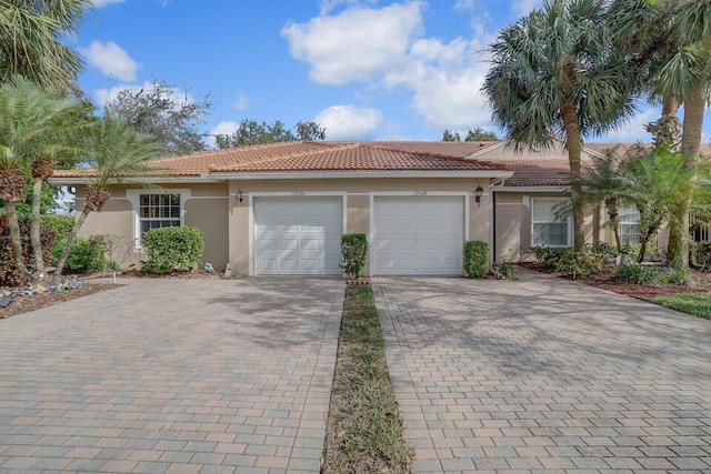 view of front of property with a tiled roof, decorative driveway, an attached garage, and stucco siding