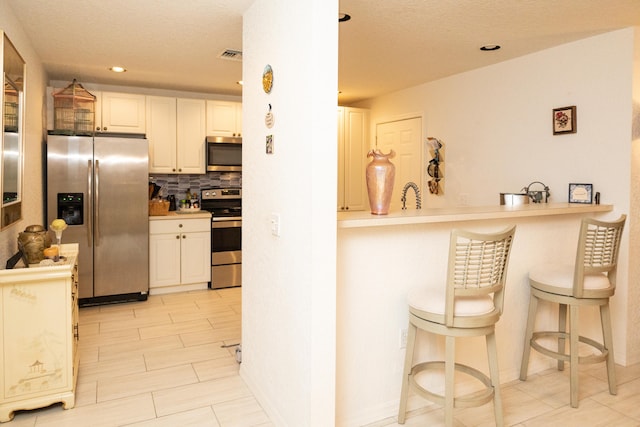 kitchen with backsplash, a breakfast bar area, white cabinetry, kitchen peninsula, and stainless steel appliances