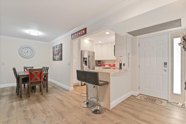 kitchen with a breakfast bar, kitchen peninsula, stainless steel refrigerator with ice dispenser, ornamental molding, and white cabinetry