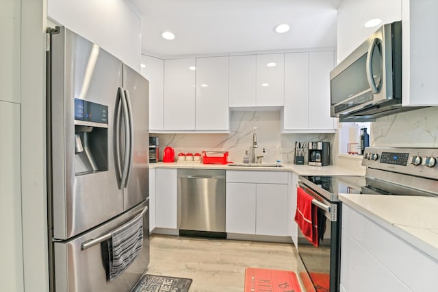 kitchen with white cabinetry, sink, decorative backsplash, appliances with stainless steel finishes, and light wood-type flooring