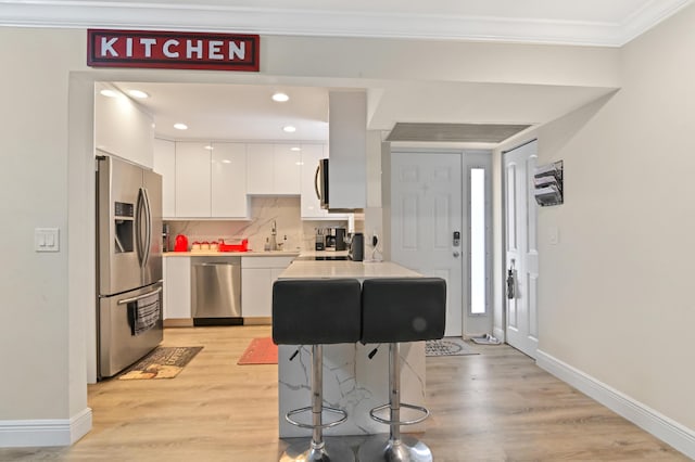 kitchen with light hardwood / wood-style floors, white cabinetry, crown molding, and appliances with stainless steel finishes