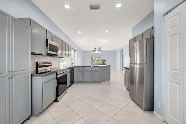 kitchen featuring gray cabinetry, light tile patterned floors, appliances with stainless steel finishes, a notable chandelier, and kitchen peninsula