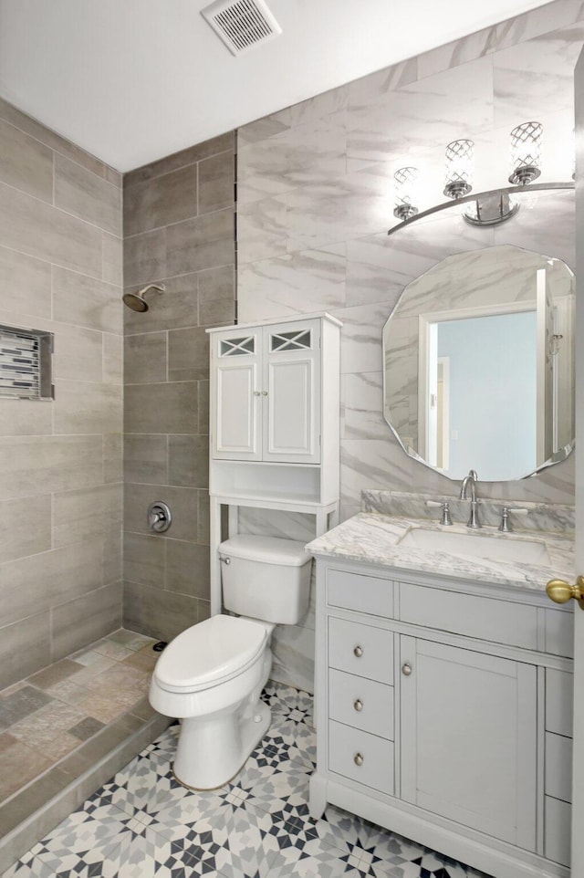 bathroom with a tile shower, tile patterned flooring, vanity, and toilet