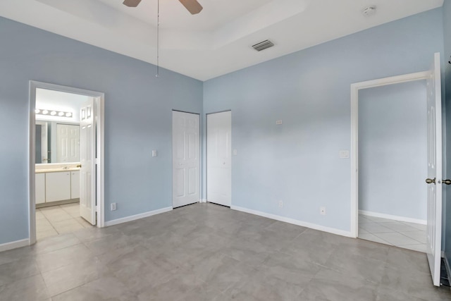 unfurnished bedroom featuring light tile patterned floors, connected bathroom, a tray ceiling, and ceiling fan