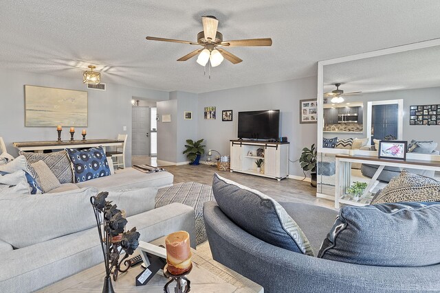 living room with ceiling fan, a textured ceiling, and light hardwood / wood-style floors