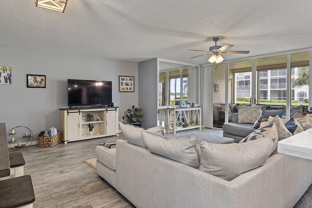 living room featuring ceiling fan, wood-type flooring, a textured ceiling, and a wall of windows