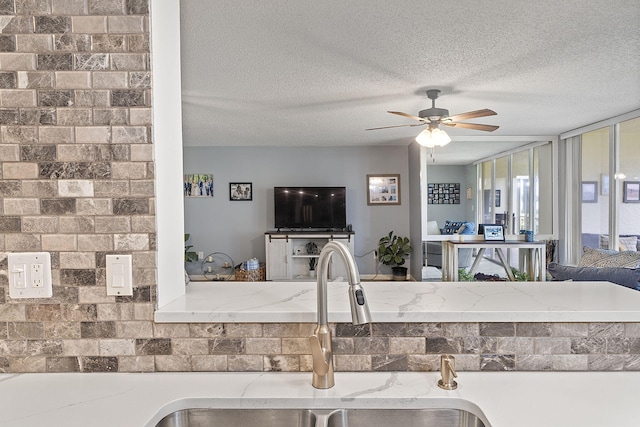 kitchen featuring light stone counters, sink, a textured ceiling, and ceiling fan