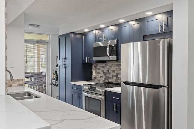 kitchen featuring appliances with stainless steel finishes, sink, decorative backsplash, light stone counters, and a textured ceiling