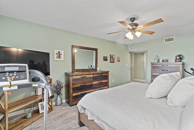 bedroom with ceiling fan, light hardwood / wood-style floors, a closet, and a textured ceiling