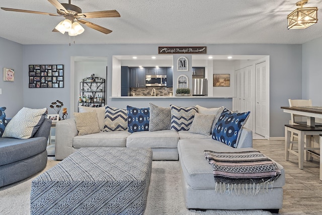 living room with ceiling fan, a textured ceiling, and light wood-type flooring