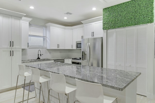 kitchen with light stone counters, a breakfast bar, stainless steel appliances, white cabinets, and a center island